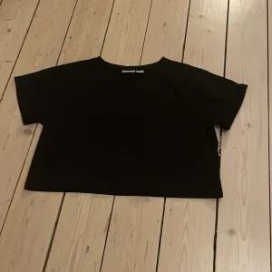 Svart croppad topp från Gina Tricot - Säljer en stilren svart croppad topp från Gina Tricot. Toppen har korta ärmar och en enkel design som passar perfekt till olika outfits. Perfekt för dig som gillar en minimalistisk stil.