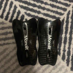 Svarta benskydd från Monolit (S) - Säljer ett par svarta benskydd från Monolit i kolfiber. . Perfekta för fotbollsspelare som söker lättviktsskydd med hög hållbarhet. 2 repor på sista bilden! Annars väldigt fina. (FODRAL MEDFÖLJER)