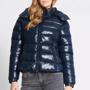 Mörkblå glansig pufferjacka - Snygg mörkblå pufferjacka med glansig finish och dragkedja framtill. Säljer den då den inte används mer och inga skador på jackan.