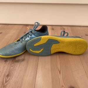  fotbollsskor från Adidas - Blå fotbollsskor från Adidas med gula detaljer och snörning. Perfekta för inomhusspel med en slitstark sula. Skorna har en bekväm passform.
