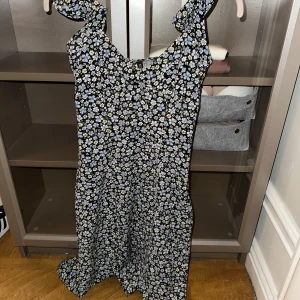 Blommig långklänning med knytband - Säljer en söt långklänning med blommigt mönster i svart och vitt. Klänningen har knytband vid axlarna och en luftig passform. Perfekt för sommarens varma dagar!