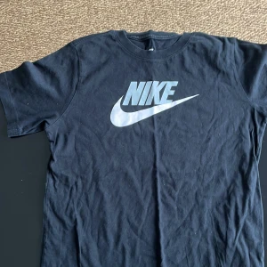 Svart t-shirt från Nike - Säljer en klassisk svart t-shirt från Nike med det ikoniska logotyptrycket i vitt på bröstet. Perfekt för en sportig och avslappnad stil. Tillverkad i mjuk bomull för extra komfort. Barn xl är storleken