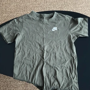 Grön t-shirt från Nike - Säljer en grön t-shirt från Nike med korta ärmar och klassisk rund hals. T-shirten har en vit Nike-logga på bröstet. Perfekt för en avslappnad stil.