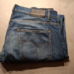 Blå jeans med slitna detaljer - Säljer ett par klassiska blå jeans med slitna detaljer. De har en rak passform och är tillverkade i denim. Perfekta för en avslappnad stil. TOS Pistolero. Säljs billigt pga lilla hålet ni kan se, lätt o laga.