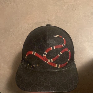  Gucci keps - Snygg svart snake keps från Gucci med ett iögonfallande ormmotiv i rött och vitt. Kepsen har ett diskret mönster och justerbar rem baktill med röd och blå detalj. Perfekt för att ge din outfit en lyxig touch. Priset kan diskuteras vid snabbaffär byte funkar bara mot tiger gucci keps eller den blåa original