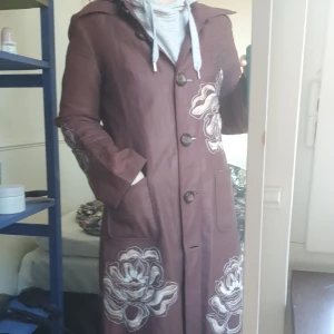 Brun retro kappa med broderi - Brun vårkappa med broderade blommor. Äkta retro H&M helt utan skavanker. Så fin!! Men kommer tyvärr inte till användning hos mig. Passar 36-38. Ganska tunn.