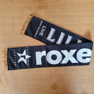 ROXETTE ~Join the joyride tour scarf |turnéhalsduk oanvänd svensk pop rock  - ROXETTE Join the joyride tour scarf |turnéhalsduk svensk pop   Status Quo   Storlek ca 90 x 15 cm.  Sida1: Lilli och Sussie Sida2: ROXETTE | Snygg svart halsduk med vit text och guldfransar. Texten inkluderar 'LIVE', 'SAVE THE WORLD' och 'roxette'. Perfekt för fans och samlare.