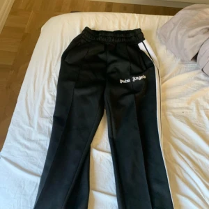 Svarta byxor från Palm Angels - Snygga svarta byxor från Palm Angels med vit sidoremsa och elastisk midja. Byxorna har en avslappnad passform och dragsko i midjan för extra komfort. Perfekta för en stilren look.