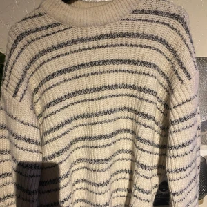 Randig stickad tröja från DeFacto - Mysig stickad tröja från DeFacto i beige med svarta ränder. Perfekt för kyliga dagar med sin ribbade krage och långa ärmar. En klassisk och stilren design som passar till mycket.