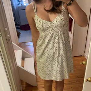 Vit prickig klänning med knytband - Säljer en superfin vit klänning med små svarta prickar. Den har smala axelband och ett sött knytband i ryggen. Perfekt för sommardagar eller en avslappnad fest. Klänningen är i bra skick och har en luftig passform. Skriv för fler frågor!🤍
