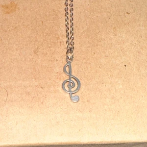 Silverfärgat halsband med G-klav - Säljer ett snyggt silverfärgat halsband med en hängande G-klav. Perfekt för musikälskare! Kedjan är tunn och elegant, vilket gör det lätt att bära till både vardags och fest.