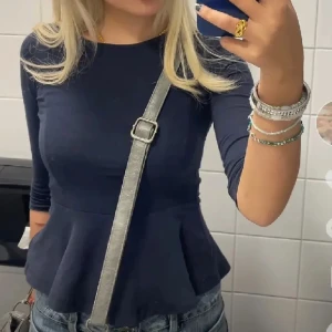 Mörkblå topp med peplum från Bik Bok - Säljer en snygg mörkblå topp från Bik Bok med peplumdetalj i midjan. Toppen har långa ärmar och en rund halsringning. Perfekt för både vardag och fest!