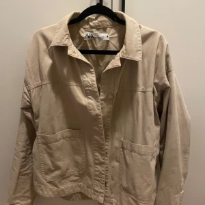 Beige jacka från Zara - Säljer en snygg beige jacka från Zara i storlek S. Jackan har en avslappnad stil med stora fickor framtill och knappar. Perfekt för vår och höst! Har inte använt så mycket, inte min stil