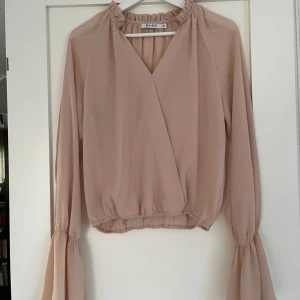 Champagnefärgad/beige blus från NA-KD - Campagnefärgad/beige blus med liten rysshad krage och trumpetärmar från NA-KD i storlek 36. Använd vid ett fåtal tillfällen. 