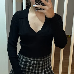 Svart ribbad v-ringad topp - Säljer en snygg svart ribbad topp med v-ringning. Den har långa ärmar och en tight passform, perfekt för både vardag och fest. Toppen är stilren och lätt att matcha med olika outfits.