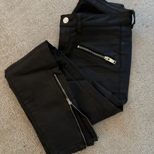 Skinnbyxor - Byxor i läder/läderimitation med dragkedjor. Storlek 26. Aldrig använda. 