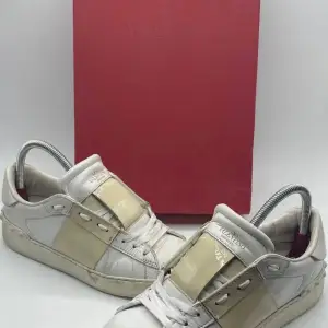 Säljer ett par snygga Valentino sneakers i vitt och beige. Skorna har en stilren design med en bred beige rem över snörningen. De är i välanvänt skick med synliga tecken på användning, speciellt på sulorna. Perfekta för en casual look med en touch av lyx.