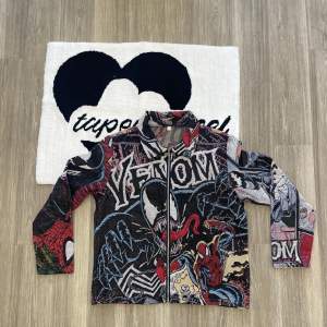 Säljer en supercool flerfärgad jacka med Venom- och Spiderman-motiv. Jackan har en dragkedja framtill och är långärmad. Perfekt för dig som vill sticka ut med en unik stil! Den är i bra skick och passar perfekt för höst och vår.