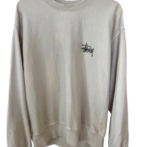Grå sweatshirt från Stussy - Basic LS tee från Stussy i storlek S. Tröjan är ”oversized” med långa ärmar och ribbade muddar. Den har Stussy-loggan tryckt både fram och bak, vilket ger den en cool streetwear-look. Perfekt för både vardag och chill.