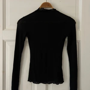 Svart ribbad långärmad topp - Säljer en stilren svart ribbad långärmad i tunt material, långa ärmar och sköldpaddskrage. Perfekt basplagg som passar för både vardag och fest! Den har en tight passform som framhäver figuren och är superbekväm att ha på sig.