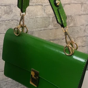 Grön axelväska med gulddetaljer - Säljer en superfin grön axelväska i skinn med gulddetaljer. Väskan har en stilren design med en praktisk dragkedja och ett snyggt spänne framtill. Perfekt för både vardag och fest!