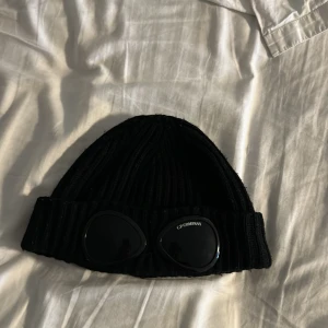 Svart stickad mössa med glasögondetalj - Säljer en svart stickad mössa från C.P. Company. Använd förra vinter. Pris går att diskuteras vid snabb affär går också att byta. (Äkta) kvitto borta köpt på nk 