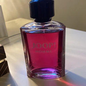 Joop! Homme Eau de Toilette - Säljer en flaska Joop! Homme Eau de Toilette. Den har en cool, fyrkantig design med en djup rosa färg på vätskan. Flaskan har en svart kork och ser riktigt stilren ut. Perfekt för dig som vill ha en doft som sticker ut!