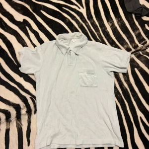 Ljusblå pikétröja - Säljer en ljusblå pikétröja i frotté. Den har en klassisk krage och en liten bröstficka. Perfekt för en avslappnad stil. Tröjan är i ok skick och passar till både vardag och lite finare tillfällen.