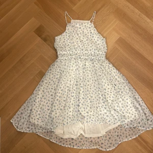 Vit blommig klänning från H&M - Säljer en superfin vit klänning från H&M med små blå blommor. Den har smala axelband och en elastisk midja som ger en bekväm passform. Perfekt för sommarens alla fester eller en mysig dag i solen. Klänningen är i nyskick, bara använt en gång 🌸