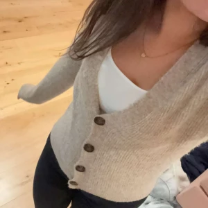 Beige stickad kofta från Neo Noir - Säljer en superfin beige stickad kofta från Neo Noir. Den har en v-ringad design med stora, snygga knappar framtill. Perfekt för höst och vinter, och den är både mysig och stilren. Passar perfekt till både jeans och kjol!