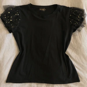 T-shirt  - Svart T-shirt med guldiga detaljer vid puffärmen. 