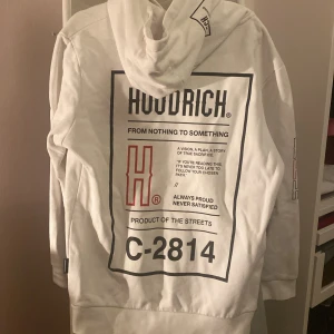 Vit hoodie från Hoodrich - Säljer en snygg vit hoodie från Hoodrich. Den har en stor logga på framsidan och en cool design på baksidan med texten 'From Nothing to Something'. Hoodien har en känguruficka och ribbade muddar vid ärmslut och nederkant. Perfekt för en avslappnad stil!