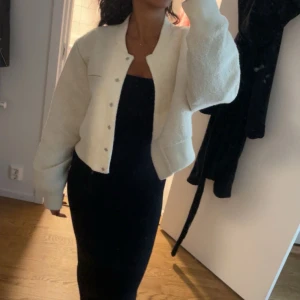 Vit jacka med knappar - Säljer en superfin vit jacka med knappar framtill. Den är perfekt för både höst och vår, och har en snygg, croppad passform. Jackan är långärmad och ser riktigt mysig ut. Perfekt att ha över en klänning eller till jeans för en stilren look!