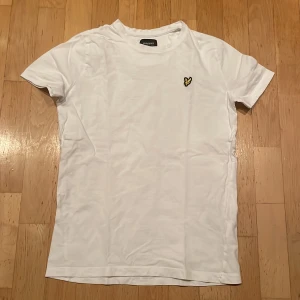 Vit t-shirt från Lyle & Scott Junior - Säljer en snygg vit t-shirt från Lyle & Scott Junior. Den har en liten broderad Lyle & Scott logga. Perfekt för en stilren och enkel look. T-shirten är i bomull och har korta ärmar. Passar perfekt till både vardag och fest