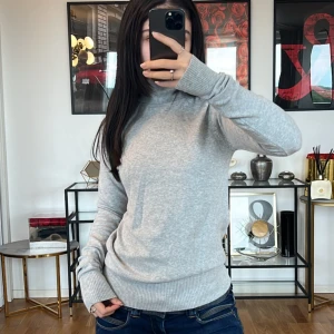 Grå polotröja - Säljer en supermysig grå polotröja i mjukt material. Perfekt för kyliga dagar med sin höga krage och långa ärmar. Tröjan har en normal passform och ribbade muddar vid ärmslut och nederkant. Passar perfekt till både jeans och kjol för en avslappnad look.