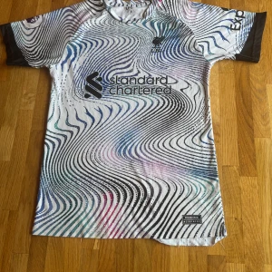 Liverpool FC fotbollströja med M. Salah 11 - Säljer en supercool Liverpool FC fotbollströja från Nike med M. Salahs namn och nummer 11 på ryggen. Tröjan har ett unikt svartvitt mönster med vågiga linjer och är kortärmad. Perfekt för alla Liverpool-fans!