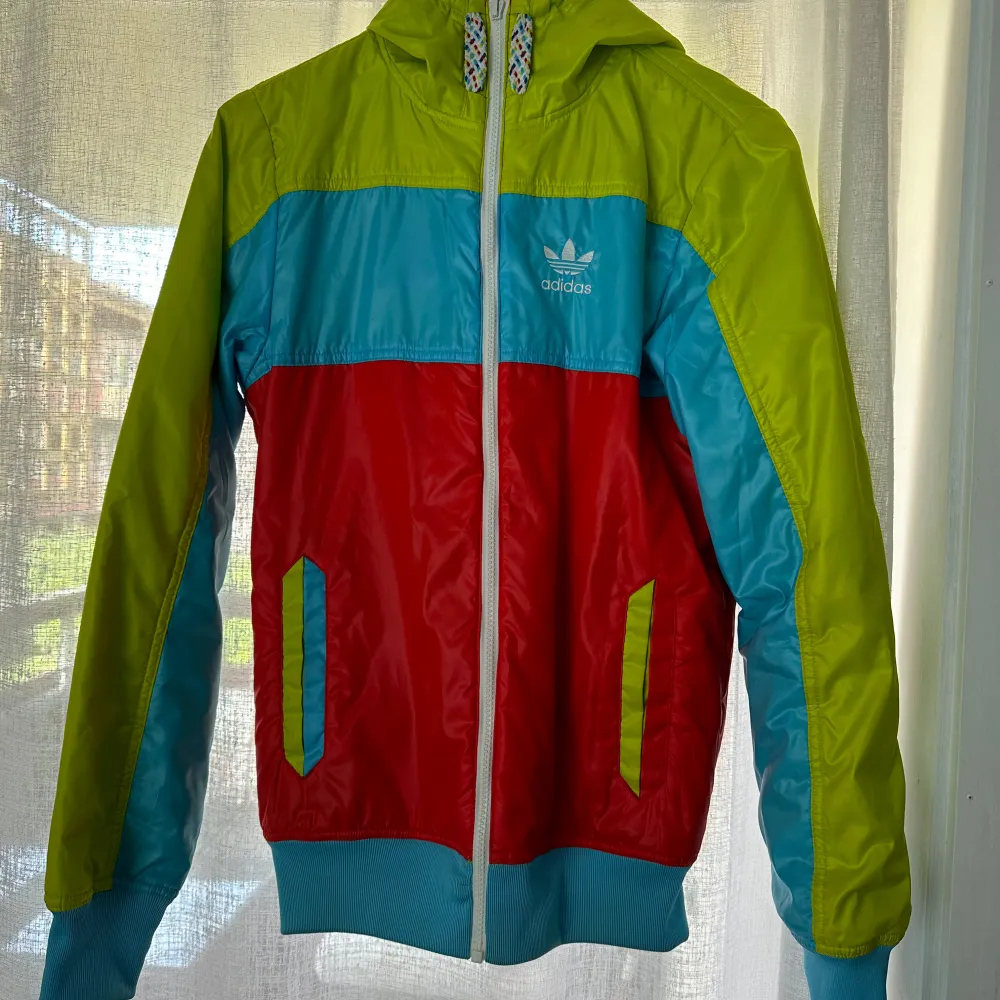 Säljer en supercool och färgglad vindjacka från Adidas. Jackan har en mix av limegrön, turkos och röd färg som verkligen sticker ut. Den har en dragkedja framtill och en huva med färgglada snören. Finns i XS och L. Jackor.