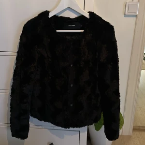 Svart pälsjacka från Vero Moda - Säljer en supermjuk och fluffig svart pälsjacka från Vero Moda. Perfekt för att hålla sig varm och stilren under kyliga dagar. Jackan har långa ärmar och stängs med knappar framtill. Den är i mycket bra skick och passar perfekt för höst och vinter. 🖤
