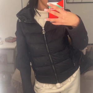 Svart dunjacka med huva - Säljer en snygg svart dunjacka från Moncler. Den har en dragkedja framtill och en praktisk huva. Jackan är perfekt för kyliga dagar och har en tight passform som ger en stilren look. Den är i mycket bra skick och passar perfekt för både höst och vinter.