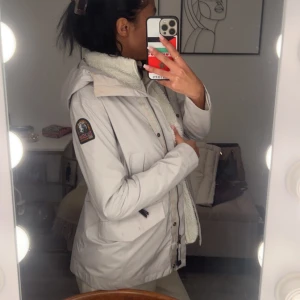 Vit jacka från Parajumpers - Säljer en snygg vit jacka från Parajumpers. Den har en mysig fodrad insida och en praktisk huva. Perfekt för kyliga dagar! Jackan har både dragkedja och knappar för extra skydd mot väder och vind. Den är i mycket bra skick och redo för nya äventyr. Vid snabb affär kan vi diskutera pris😀