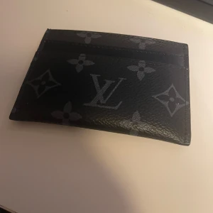 Svart kortfodral från Louis Vuitton - Säljer ett stilrent svart kortfodral från Louis Vuitton med det klassiska monogrammönstret. Perfekt för att hålla dina kort organiserade med stil. Tillverkat i Frankrike och i mycket bra skick. Passar perfekt för både vardag och fest!