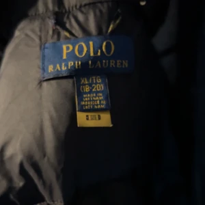 Svart dunjacka från Polo Ralph Lauren - Säljer en svart dunjacka från Polo Ralph Lauren i storlek XS Jackan är perfekt för kalla vinterdagar med sin tjocka vaddering och stilrena design. Den har en dragkedja framtill och flera praktiska fickor. Passar både till vardags och mer uppklädda tillfällen. Kom dm för fler bilder, kan gå ner lite i pris vid snabb affär. Den har några små hål i armarna men inget man märker så tydligt.