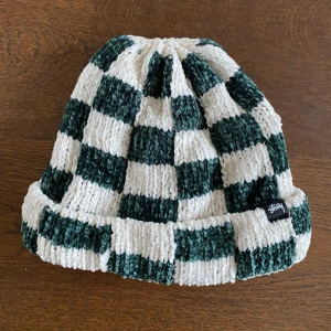Rutig stickad mössa från Stussy - Säljer en supercool rutig mössa från Stussy i grönt och vitt. Den är stickad och perfekt för att hålla dig varm under höst och vinter. Mössan har en normal passform och är i mycket bra skick. Perfekt för att ge din outfit en extra edge!