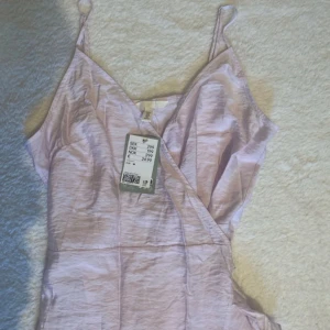 Ljuslila långklänning - Säljer en elegant ljuslila långklänning med smala axelband och omlott-design. Perfekt för sommarens fester eller en fest kväll. Klänningen har en v-ringad urringning och är i ett mjukt, glansigt material som ger en lyxig känsla. Helt oanvänd med prislappen kvar!😍