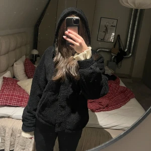 Svart teddyjacka med huva - Mysig svart teddyjacka med huva. Den är fodrad, perfekt för kyliga dagar. Jackan har långa ärmar och en avslappnad passform. Den är supermjuk och varm, passar höst och vinter. Använd 2-3 gånger, superbra skick utan några slitage.