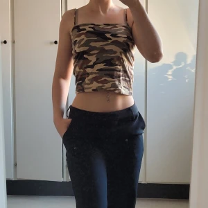 Camouflagefärgad croppad topp från Gina Tricot - Säljer en supercool camouflagefärgad croppad topp från Gina Tricot. Den har smala axelband och är perfekt för sommardagar eller festivaler. Toppen är i mycket bra skick och ger en snygg och avslappnad look. Perfekt att matcha med jeans eller shorts!