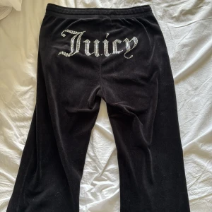 Svarta Juicy Couture mjukisbyxor - Säljer ett par svarta mjukisbyxor från Juicy Couture i mycket bra skick. Byxorna har en glittrig Juicy-logga på baksidan och snörning i midjan. Framtill så är en knapp av och ”hylsan” som sitter på snöret. Annars är dom i bra kvalite 