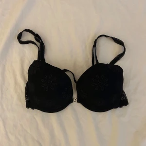 Svart broderad bh från Selmark - Snygg svart bh från Selmark med vackra broderade detaljer i strl 75 B. Den har justerbara axelband och en liten dekorativ magnetsikt spänne mellan kuporna. Bekväm och stilren design!