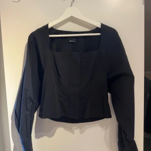 Svart långärmad topp från Bik Bok - Snygg svart topp från Bik Bok med långa ärmar och fyrkantig halsringning. Perfekt för både vardag och fest. Den har en stilren design som gör den lätt att matcha med olika outfits. 