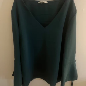 Mörkgrön blus med v-ringning - mörkgrön blus med v-ringning. Ärmarna slutar ungefär vid armbågen och har en slits där ifrån med två snören som går knytas. Inga defekter. Hör av dig vid frågor eller bild på💕💕
